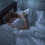 A woman sleeping peacefully in a cozy bedroom, enveloped by soft white sheets, under the gentle glow of night lighting.